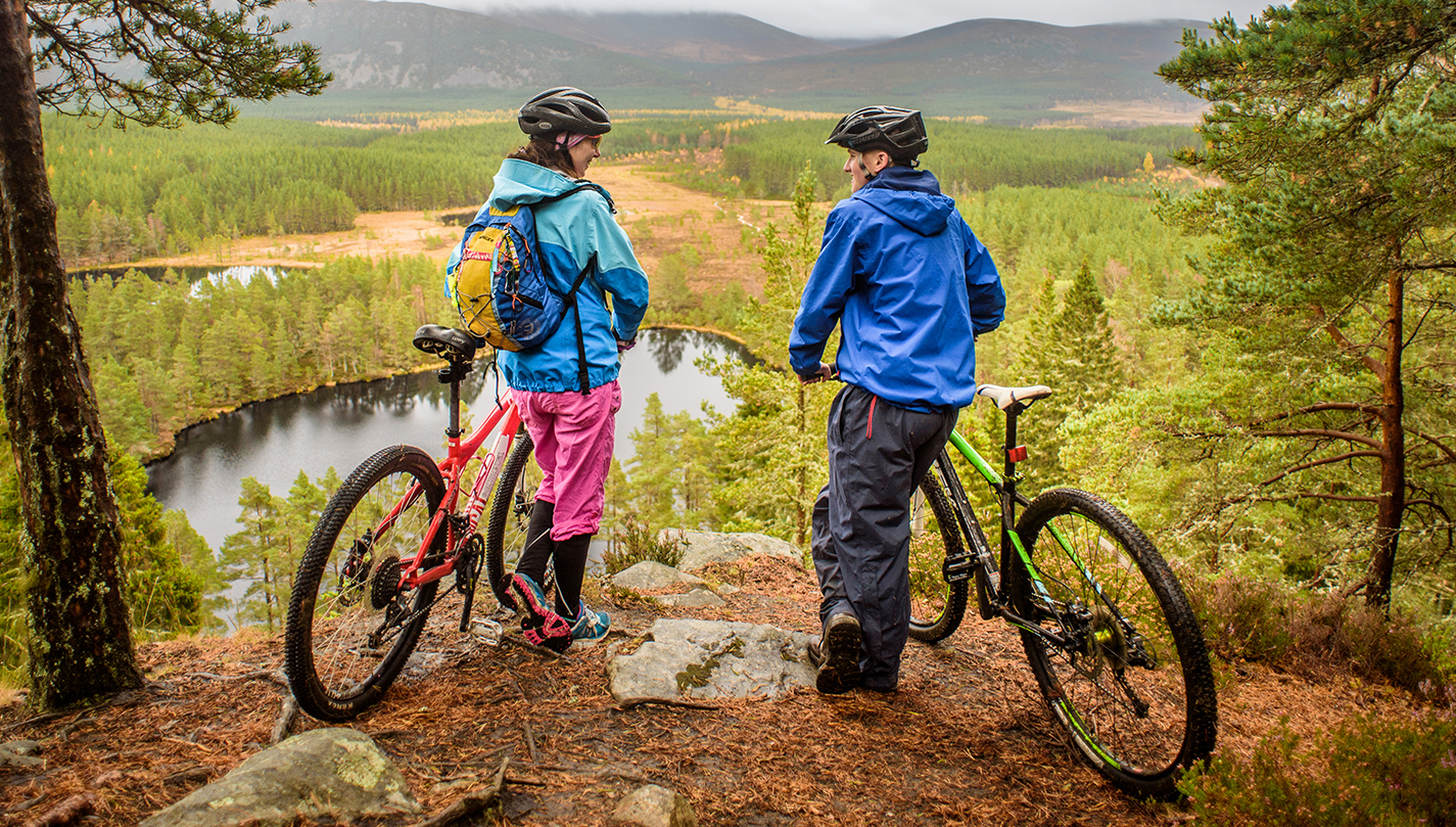 Two people holding bikes and looking over a scenic forest view